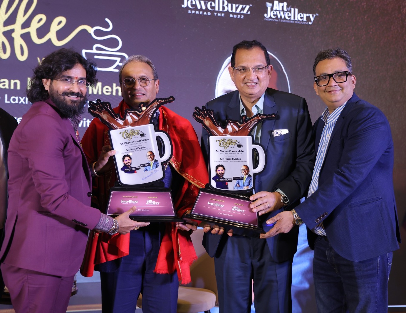 Commemorative trophies presented on stage at the Coffee with CKM conversation, in front of a backdrop naming Dr. Chetan Kumar Mehta and Mr. Russell Mehta.